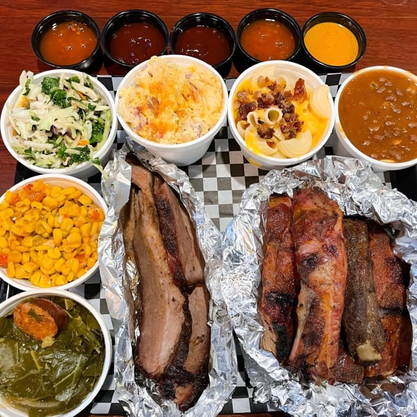 A Santa Maria BBQ spread with brisket, ribs, coleslaw, mac and cheese, corn, collard greens, and sauces.