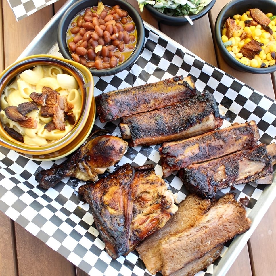 A Santa Maria BBQ platter with ribs, chicken, brisket, mac and cheese, baked beans, and corn.