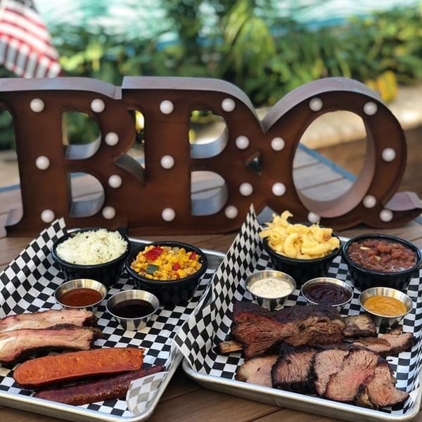 Two trays of Santa Maria BBQ with ribs, sausage, brisket, and sides like mac and cheese.