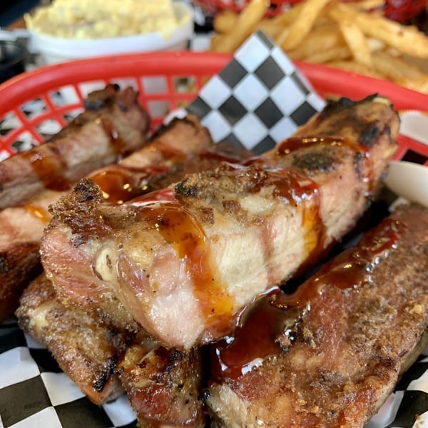 Close-up of Santa Maria BBQ ribs with sauce, served in a red basket with fries and coleslaw.