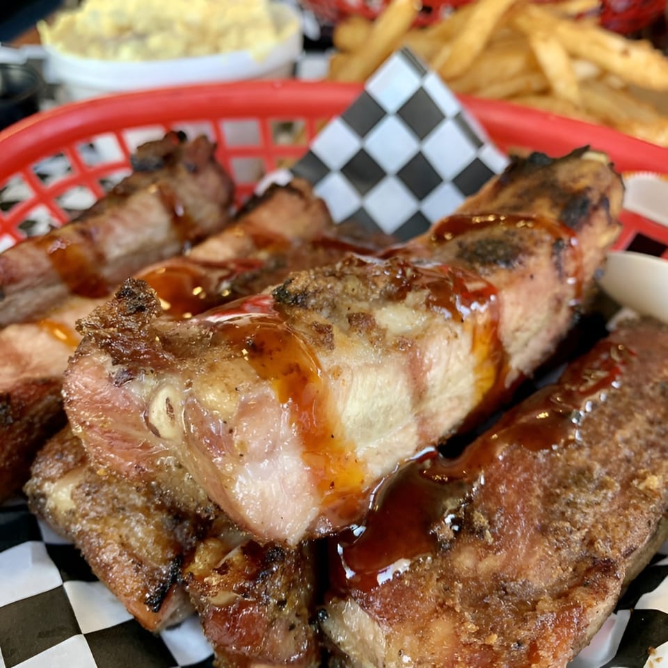 Close-up of Santa Maria BBQ ribs with sauce, served in a red basket with fries and coleslaw.